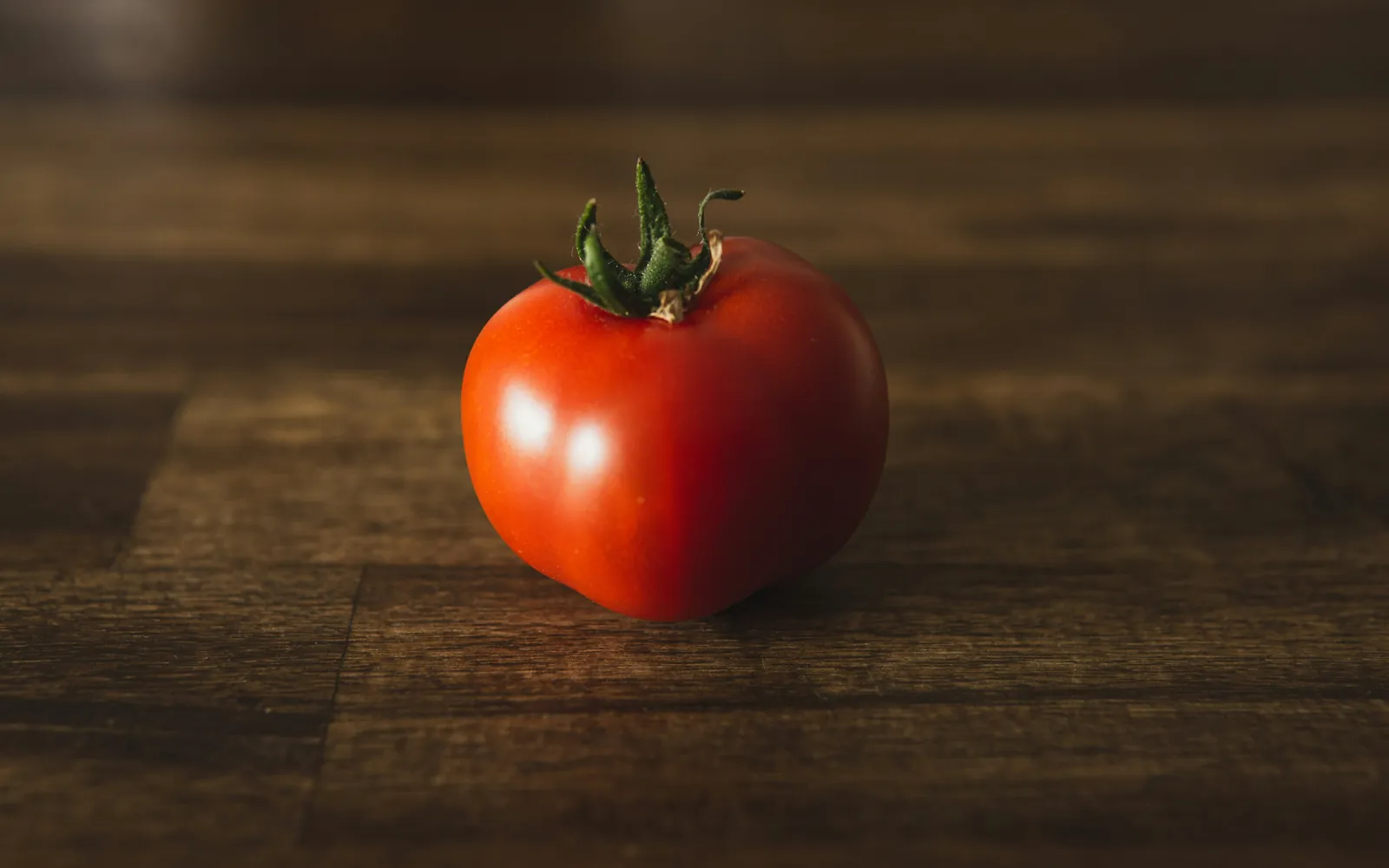 Um tomate sobre uma mesa de madeira escura